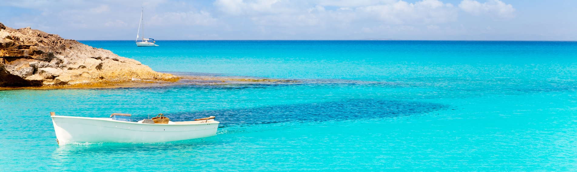A boat floats on the crystal clear sea in Formentera, Spain.